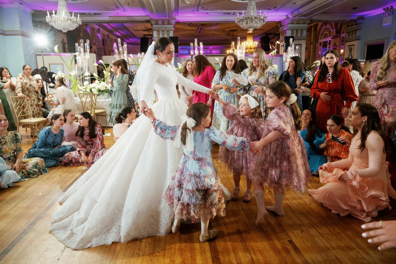 Young girls hold hands and dance around the bride while women watch and sing beside the ballroom dance floor. From this Oholei Torah Ballroom wedding. Wedding photography.