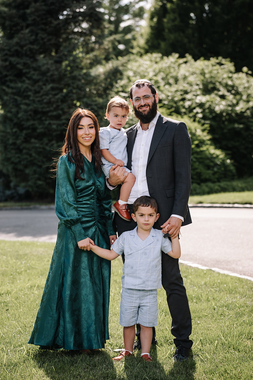 Outdoor wedding day family portrait of a couple with two boys standing on the grass in natural light.